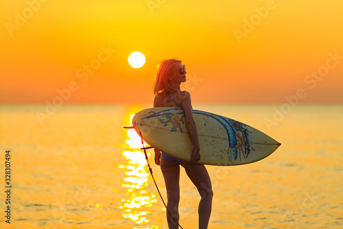夕日の海に立つサーフボードを持った白人女性