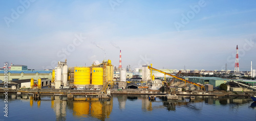 Japan - February 20, 2019: Many factory of industrial type are located near the river with clear blue sky background and above copy space. Factory emits pollutants into atmosphere. Pollution concept