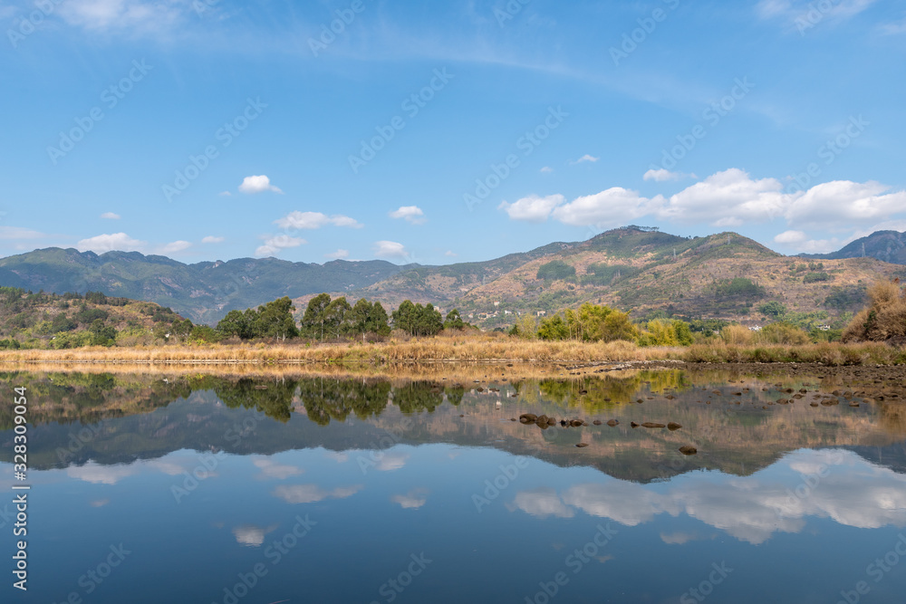 The country river reflects the mountains and trees in the distance