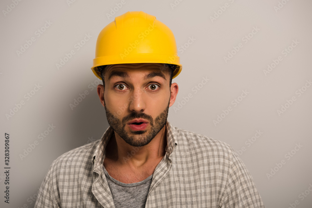 handsome shocked manual worker in yellow hardhat on grey handsome shocked manual worker in yellow hardhat on grey