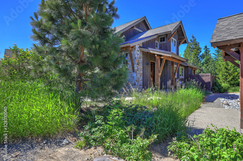 Grey wooden rustic house front exterior with pine trees and flowers and grass during summer