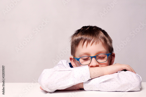 A boy with glasses is sleeping on the table. A schoolboy in uniform lies on a table with his eyes closed. Fatigue from study. Overvoltage, back to school concept. photo