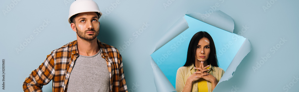 panoramic shot of pensive workman in helmet and woman in torn paper, isolated on blue panoramic shot of pensive workman in helmet and woman in torn paper, isolated on blue