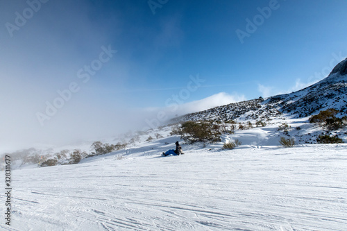 Snowboarder sitting facing foggy hill.