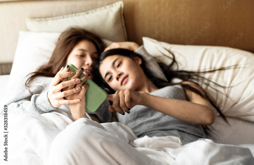 In selective focus of mobile phone was holding by love couple hands,blurred two women laying down on bed,with romantic feeling. In selective focus of mobile phone was holding by love couple hands,blurred two women laying down on bed,with romantic feeling.