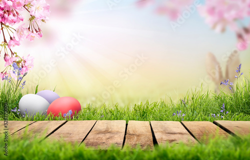 Obraz na płótnie A wooden product display top with an Easter background of painted eggs, rabbit ears, green grass, meadows and pink cherry blossom flowers. w salonie