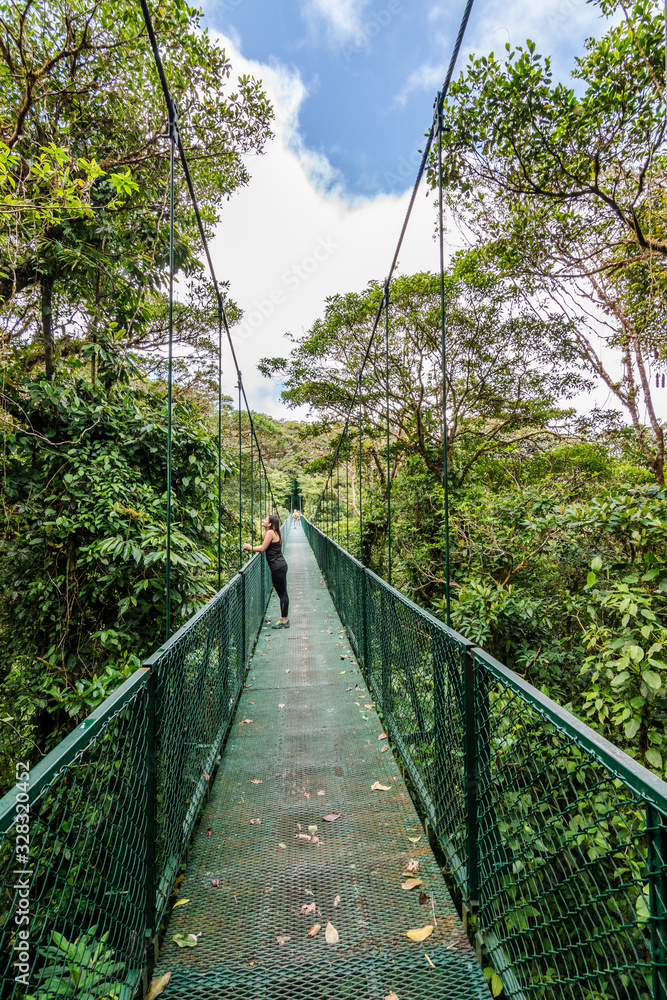 Obraz premium Woman walking in a suspension bridge during vacations in the forest