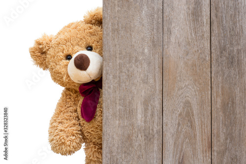 Brown cute teddy bear sneaked behind the old wooden door isolated on white background. Copy space for text and content. photo
