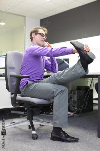  caucasian man office worker with phone in hand, stretching legs , exercising during work in call center