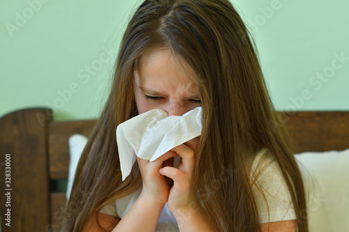 Little child girl blow his nose.Sick child with napkin in bed. Allergic kid, flu season. Kid with cold rhinitis, get cold snot nose. virus and infection