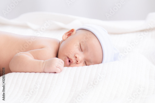 Adorable Asian newborn baby deeply sleeping smile Easter costume hat, tiny infant boy soft skin healthy sleep dream on white blanket on bed beautiful sun light, newborn baby health care concept