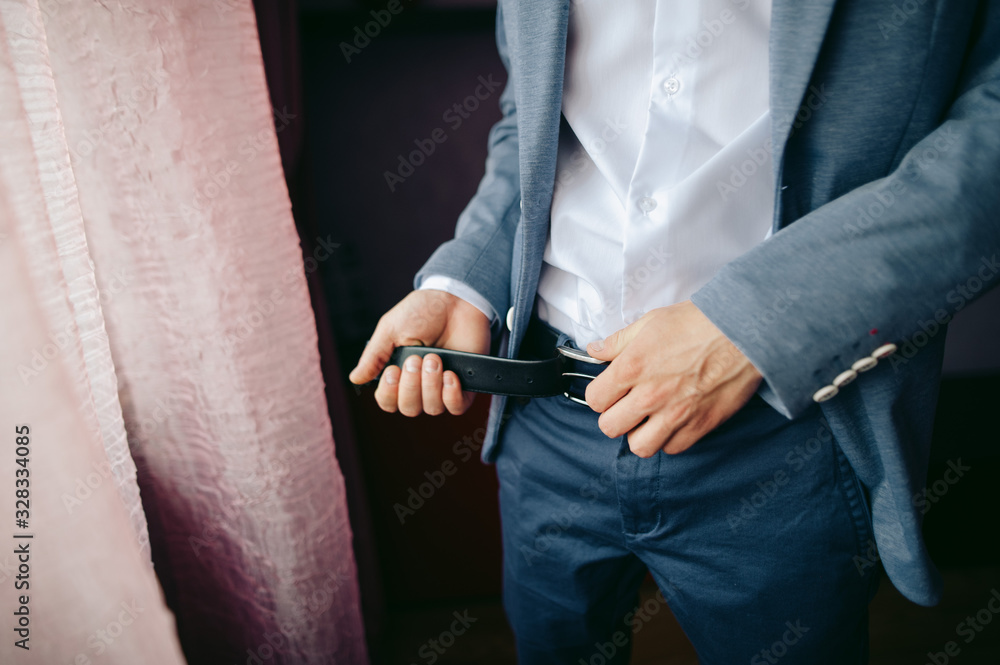 Obraz premium groom puts on a belt standing near window