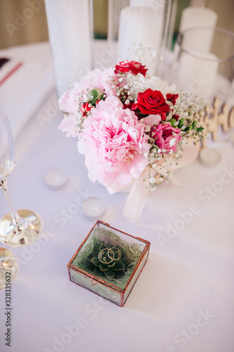 Composition of flowwers and wedding rings in a glass box with succulents are on the white table in the wedding ceremony zone