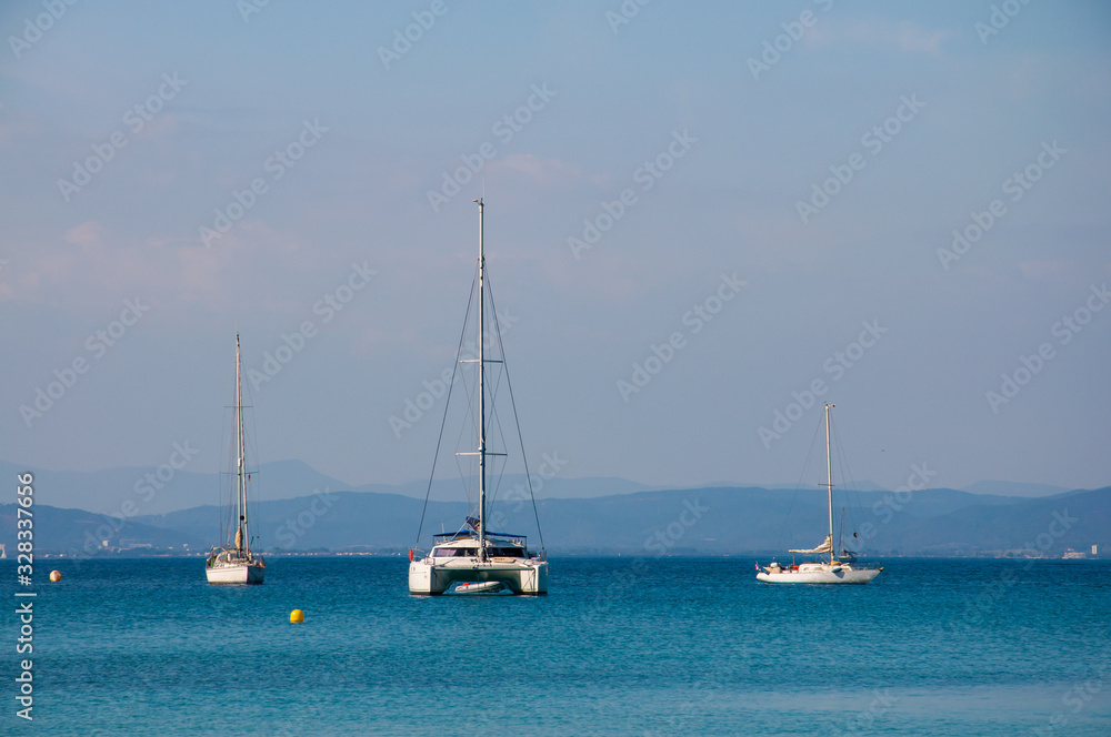 Two sailing boats and one catamaran at anchor in front of French coast. Two sailing boats and one catamaran at anchor in front of French coast.