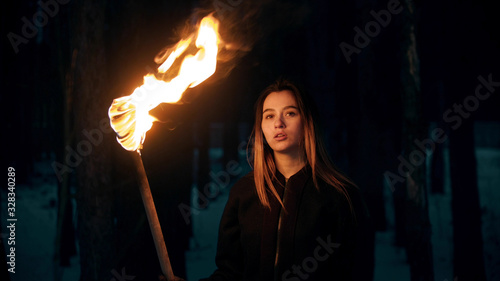 Young beautiful woman with torch in night forest photo
