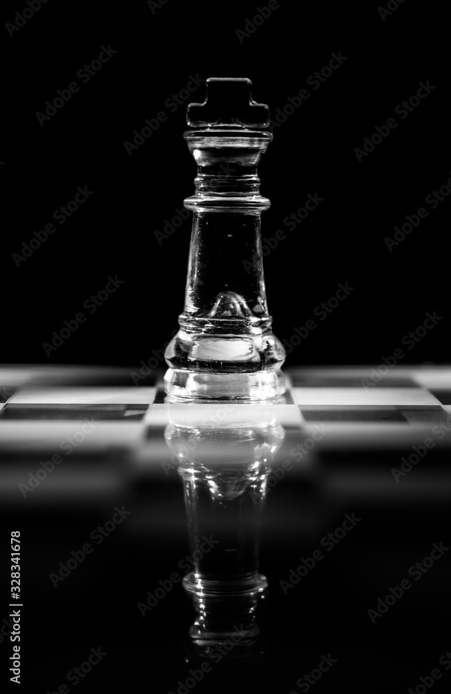 Single clear glass king chess piece or figure standing on glass chessboard with reflection. Isolated on black background with copy space. Black and white photography. Single clear glass king chess piece or figure standing on glass chessboard with reflection. Isolated on black background with copy space. Black and white photography.