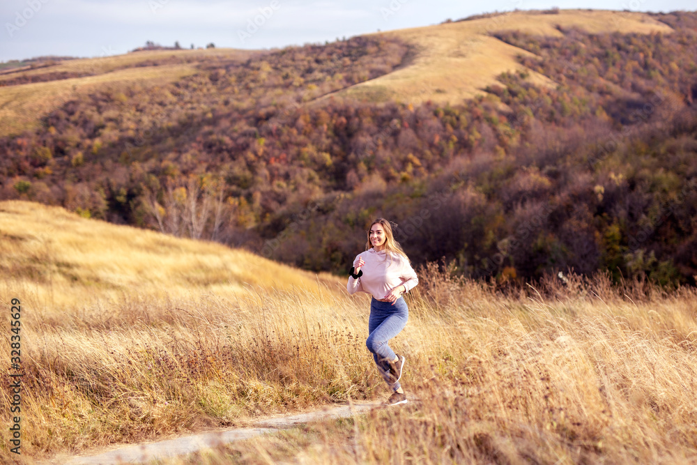 Woman in sportware running in the nature with dry grass and glade on background