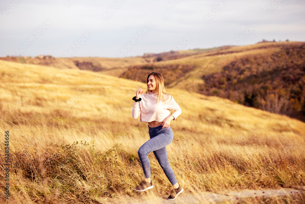 Woman in sportware running in the nature with dry grass and glade on background Woman in sportware running in the nature with dry grass and glade on background