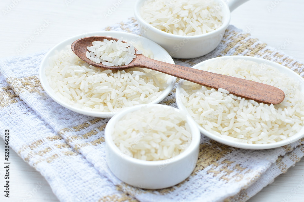 Natural raw white rice grains, on display in bowl and wooden spoon Natural raw white rice grains, on display in bowl and wooden spoon