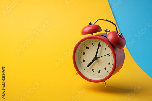 Red retro alarm clock floating in the air with yellow and blue background.