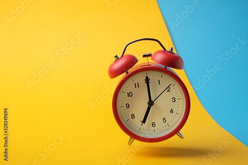 Red retro alarm clock floating in the air with yellow and blue background.