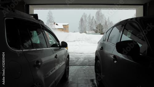 Man cleans snow with a snow thrower. View from two car from garage photo