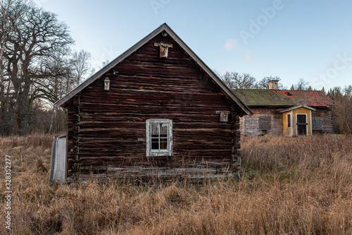 Abandoned old worn and weathered boarded wooden timber cottage house on grassy field.