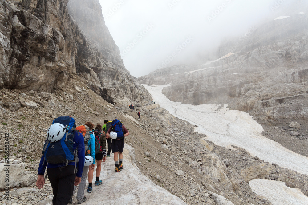 People hiking towards col Bocca del Tuckett on snow field in Brenta Dolomites mountains, Italy