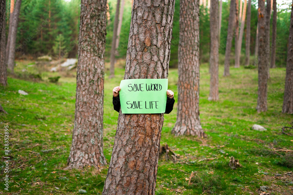Teenager holding a banner around a tree in the woods. Save world, the life. Concept of sustainability