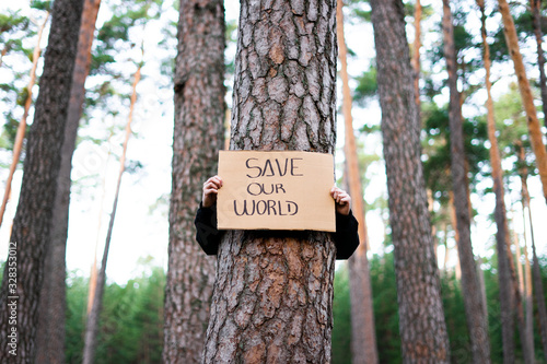 Low view of a teenage activist holding banner around a tree with a environmental message. Save our world. Concept sustainability