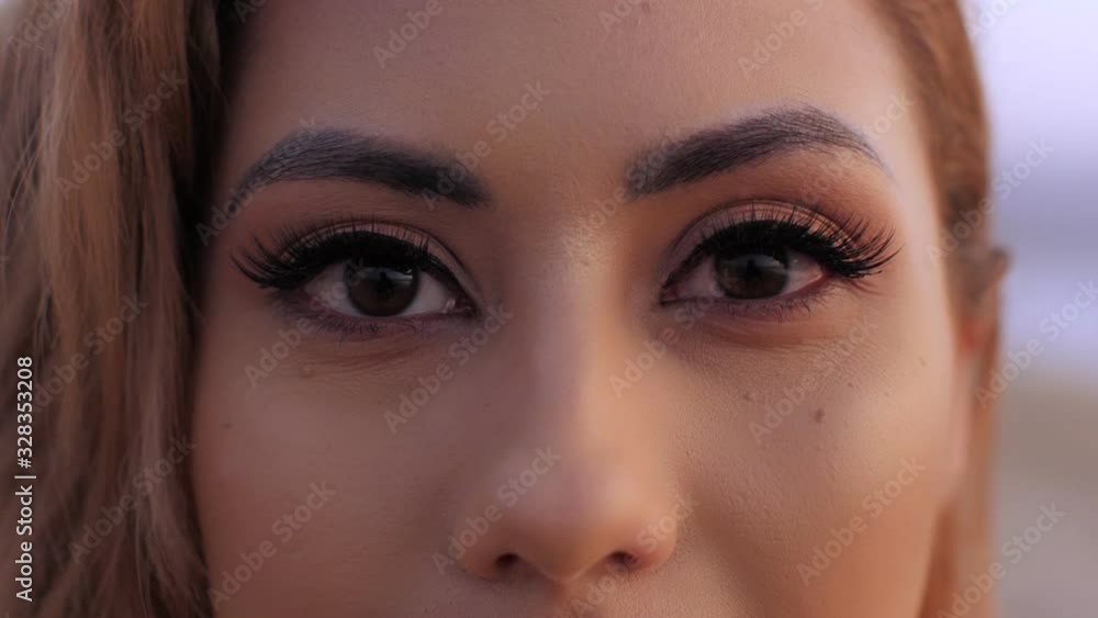 Extreme close up beautiful female hazel eyes with long lashes blinking looking at camera Extreme close up beautiful female hazel eyes with long lashes blinking looking at camera