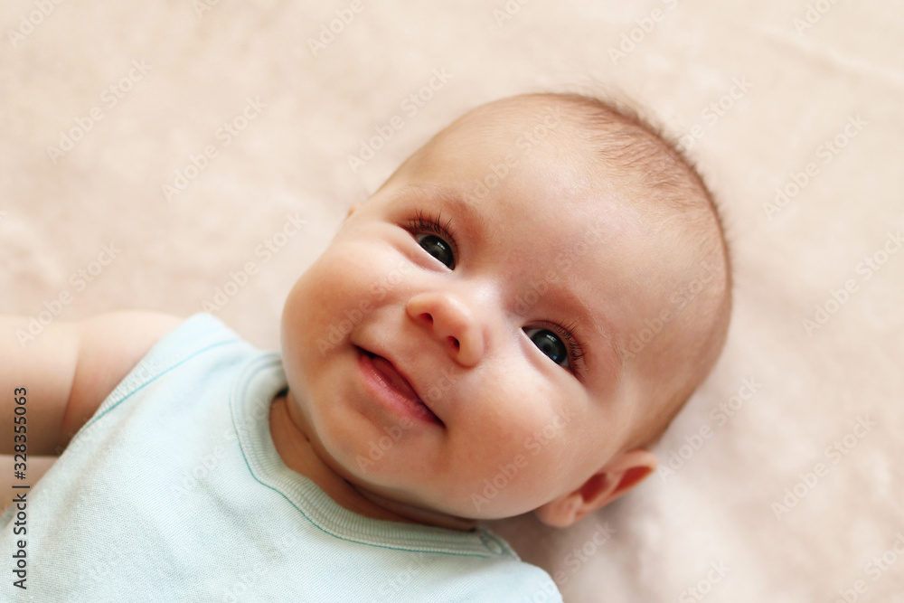 Portrait of cute smiling infant baby in blue bodysuit on a beige blanket. Portrait of cute smiling infant baby in blue bodysuit on a beige blanket.