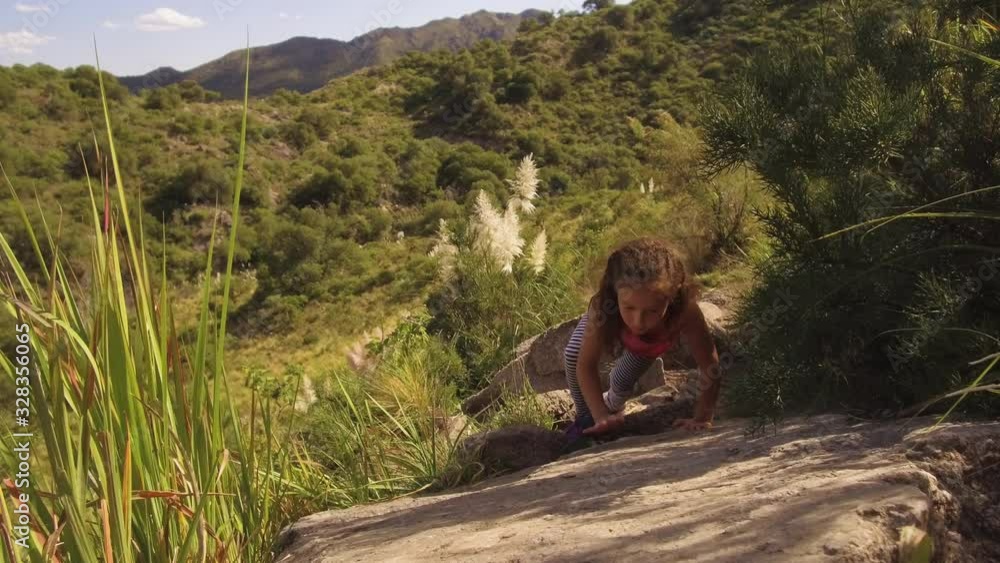 Young small girl hiking & climbing a rock- healthy active lifestyle. Hiker child walking during a trekking in beautiful mountain nature landscape. Gimbal stabilized shot. 4K. Young small girl hiking & climbing a rock- healthy active lifestyle. Hiker child walking during a trekking in beautiful mountain nature landscape. Gimbal stabilized shot. 4K.