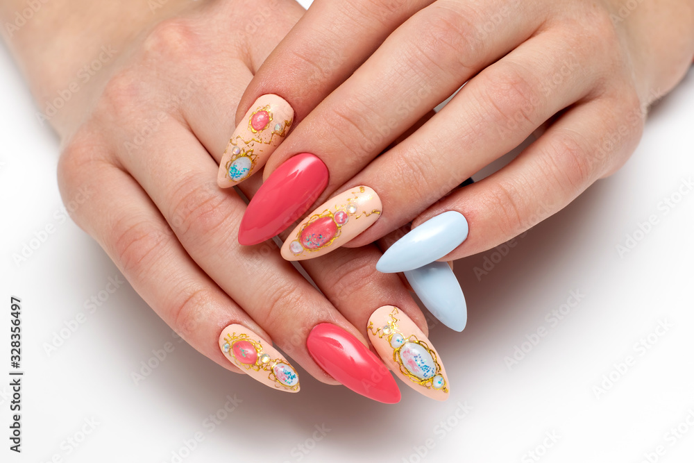 Exclusive manicure. Blue, dark blue, pink, beige, red manicure on long sharp nails. Stilettos. Falga, liquid stones, crystals, a brooch on the nails. Close up on a white background.