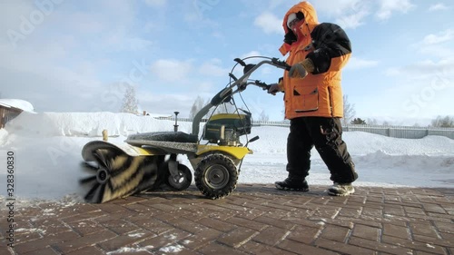 Man cleans snow in the yard with a sweeper in the winter photo