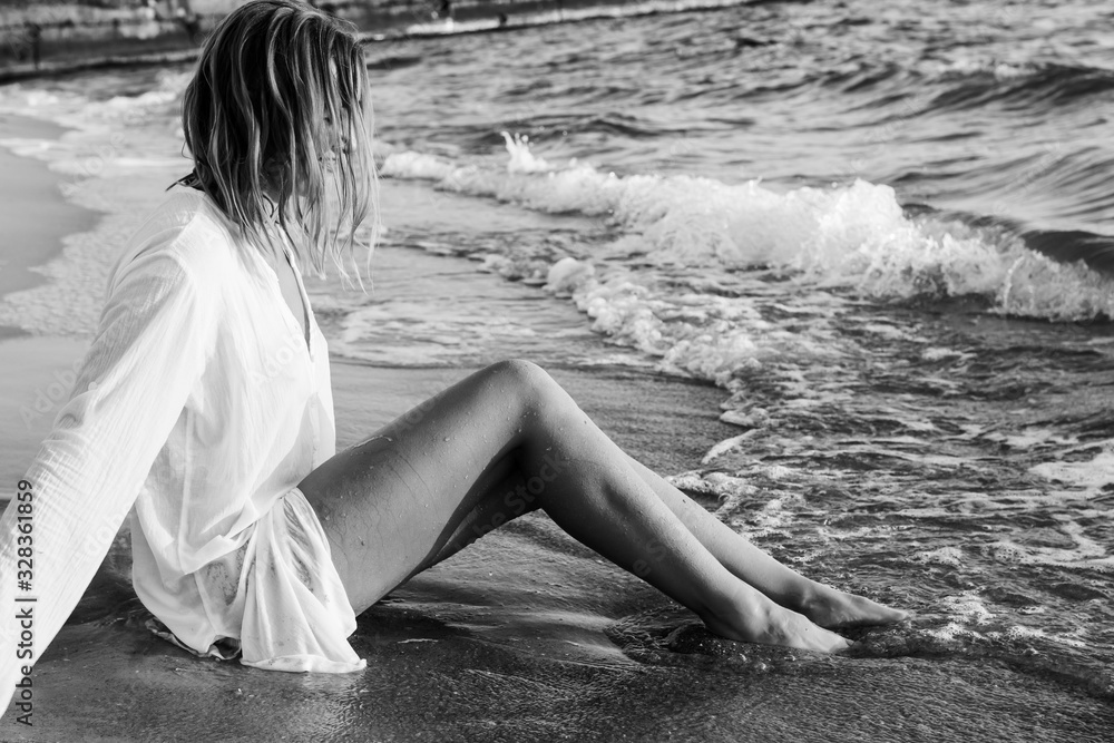 Wet Blonde Girl In White Shirt Sitting In The Water On The Sea Beach