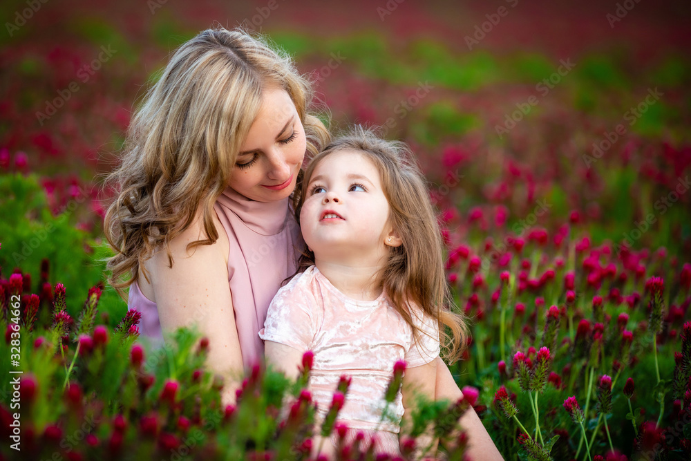 Beautiful smiling child girl with young mother in family look in field of clover flowers in sunset time Beautiful smiling child girl with young mother in family look in field of clover flowers in sunset time