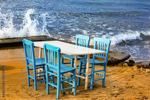 Table with four blue chaires on the beach. Waves  crashing onto the shore photo