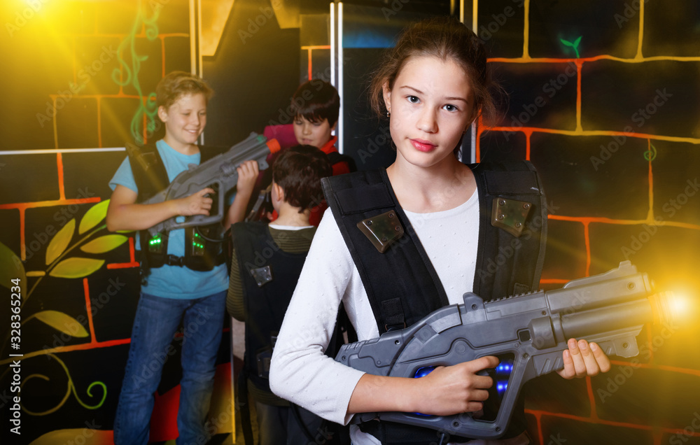 Cheerful teen girl standing with laser pistol in dark lasertag r
