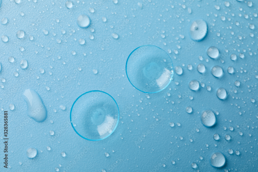 Contact lenses on blue background with water drops, top view