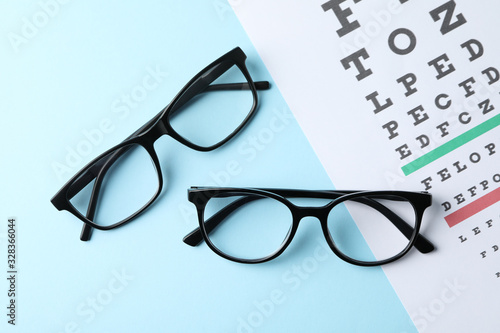 Glasses and eye test chart on blue background, top view