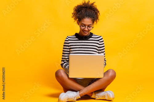 Smiling african woman using laptop computer while sitting looking aside. Copy space. Not isolated.