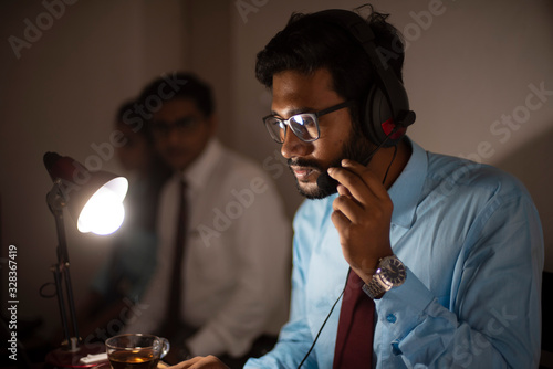 Bilde på lerret An Indian Bengali tall, dark, handsome brunette young man/tele caller in office wear is sitting on a office table in a working mood in a corporate office/bpo/call center