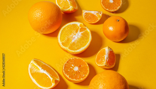 Oranges and tangerines whole and cut into pieces on a bright yellow background. Minimalistic background.