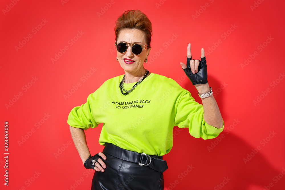 Forever Young! Elderly woman in bright outfit doing the rock sign on red background Forever Young! Elderly woman in bright outfit doing the rock sign on red background
