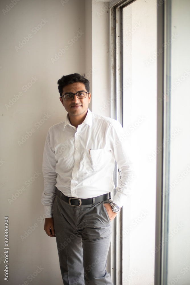 Portrait of an Indian Bengali tall, dark, handsome brunette young man in office wear is standing in front of a glass window in a corporate office/bpo/call center. Indian corporate lifestyle Portrait of an Indian Bengali tall, dark, handsome brunette young man in office wear is standing in front of a glass window in a corporate office/bpo/call center. Indian corporate lifestyle