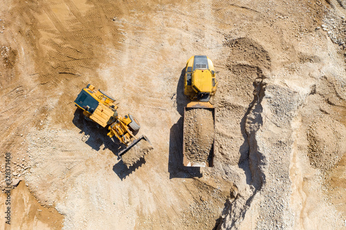 Bucket loader loading Gravel onto an Articulated hauler Truck trailer at a large construction site, Top down aerial view.