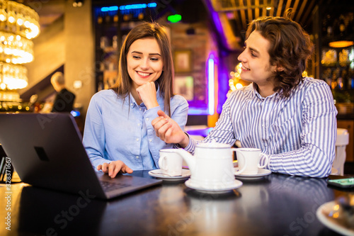 Beautiful young couple is using a laptop  talking and smiling while sitting in the cafe.