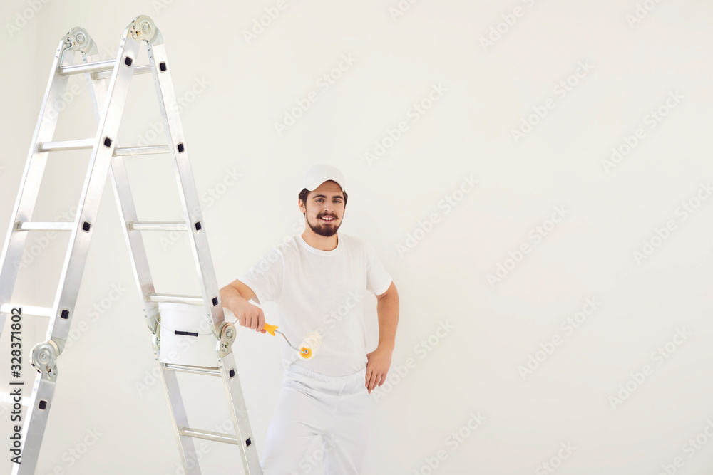 A male painter in a white uniform with a roller works in his hand in a white room A male painter in a white uniform with a roller works in his hand in a white room