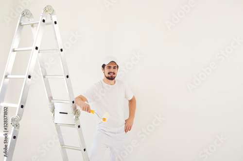 A male painter in a white uniform with a roller works in his hand in a white room